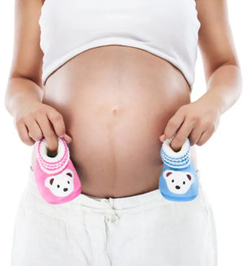 Ventre de femme enceinte entre deux paires de chaussons de bébé, une rose et une bleue
